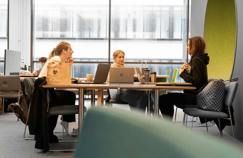 Tre tjejer som sitter vid ett bord och studerar på biblioteket.